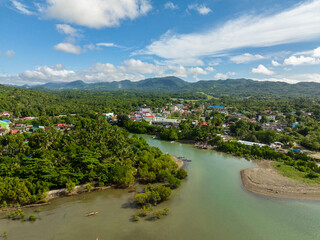 Fototapeta premium Tropical Island with houses and river. Looc, Poblacion. Blue sky and clouds. Tablas Island. Romblon, Philippines.