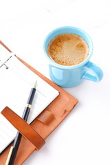 ミルクをたっぷり入れたコーヒー、カフェ・ラッテを飲みながら、茶色の革のシステム手帳でデスクワークをしているイメージ
