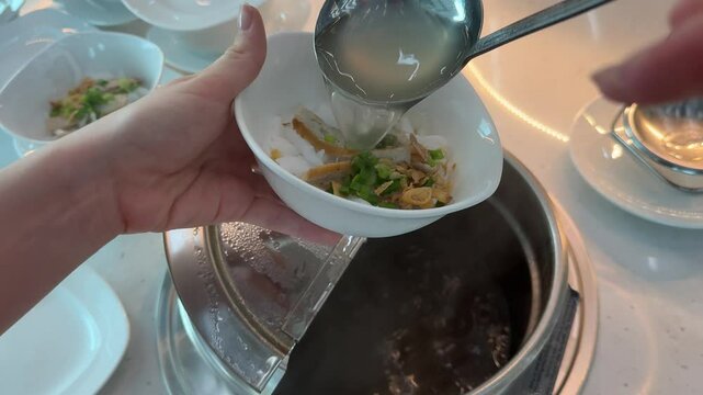 chef cooking traditional Vietnamese soup Pho-Bo, pouring tasty hot broth into bowl with rice noodles
