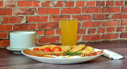 Hearty breakfast, scrambled eggs, fried bacon, pancakes, croutons, tomatoes, black coffee and orange juice on a wooden table.