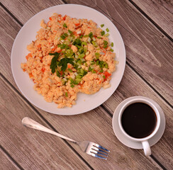 Fresh omelette with tomatoes decorated with green onions and parsley on a wooden table next to a fork and a cup of black coffee.