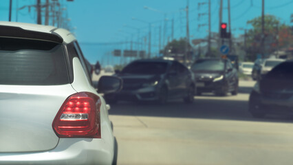 Fototapeta premium Rear side of white car on the road at day. Stop on the road with turn on brake light. Stop on the road by traffic red control. Cars on the opposite side driving through from the opposite lane.