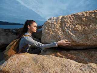 Young woman climbing on rocky terrain, showcasing determination and adventure, dressed in outdoor gear with a backpack, against a scenic landscape