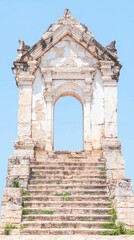 Obraz premium A weathered historical structure with an archway and worn stone steps, set against a clear blue sky.