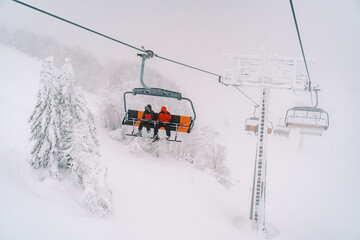 Tourists ride on a ski lift on a foggy mountain above snow-covered trees