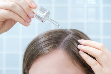 Fototapeta premium Young woman applying serum to hair with pipette on blue tile background front view.