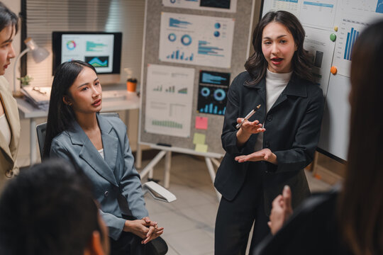 Asian businesswoman leading a meeting, presenting charts and graphs to her business team in a modern office, fostering collaboration and strategic decision-making - Powered by Adobe