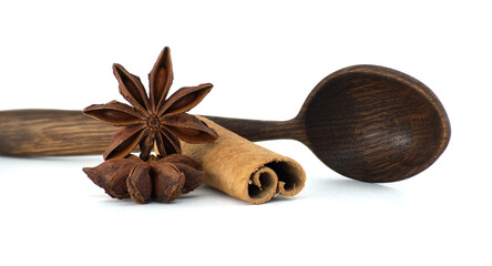 Close-up of star anise, cinnamon, and a wooden spoon create a culinary composition on white.