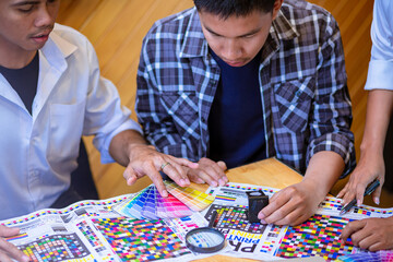 Team graphic designer checking print quality of media graphics proof print and color guides in...