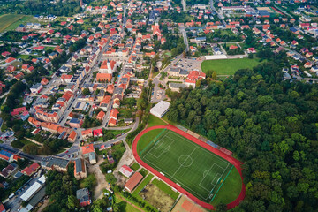 Aerial view of small European town with red roof houses, football field and green park on sunny day