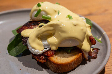 Eggs Benedict served on plate. It is a common American breakfast or brunch dish, consisting of two halves toast topped with bacon, poached egg, and hollandaise sauce.