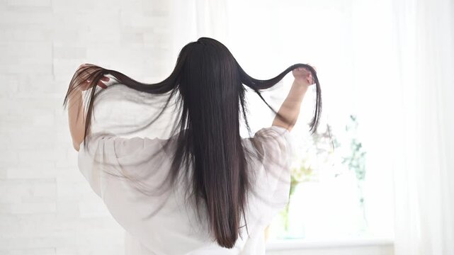 艶のあるロングヘアの黒髪の女性の後ろ姿の顔無し　キューティクルな美しいストレートヘアの髪の毛　髪の毛を持ち上げる動画