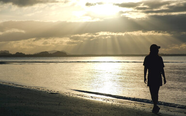 Silhouette of a woman with hat strolling on the beach in the morning