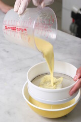 pastry chef's hand pouring batter into strainer bowl