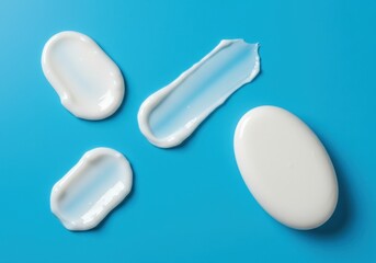 Obraz premium Four white cream smears and a soap bar on a bright blue background in a studio setting view from above