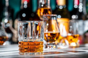 American bourbon whiskey in glass with bottles of strong drinks on dark green background
