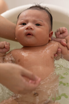 Close up asian newborn baby bathing in bathtub. mother bathing her son in warm water. Happy adorable newborn infant smile in tub relax and comfortable good moment with mom. Newborn baby care concept