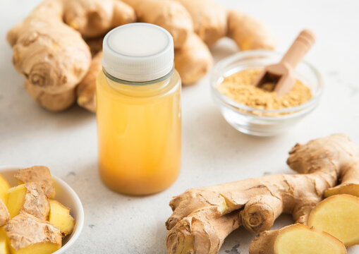 Ginger and orange energy shot immune drink with fresh raw ginger root on light background.Macro.