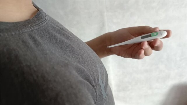 A teenage boy takes out an electronic thermometer from his armpit and looks at the temperature. Human body temperature. Acute respiratory viral infections, acute respiratory viral infections, colds, a