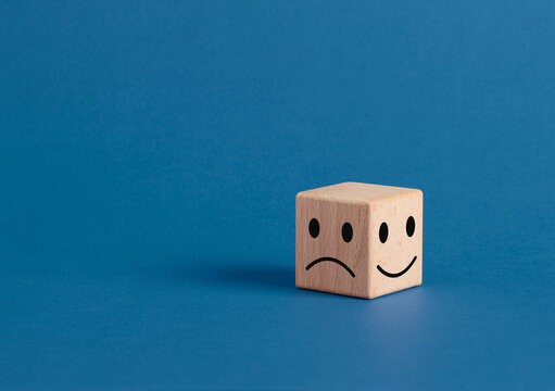 Wooden cube showing happy and sad faces expressing opposite emotions