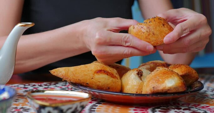 Woman breaks hot samsa in Uzbek cafe with colorful traditional setting.