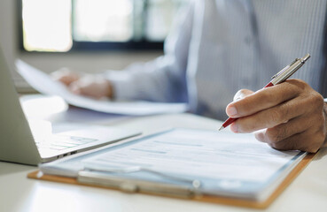 asian businessman reviewing document at office workplace with computer laptop. legal expert, professional lawyer reading and checking financial documents or insurance contract, close up shot