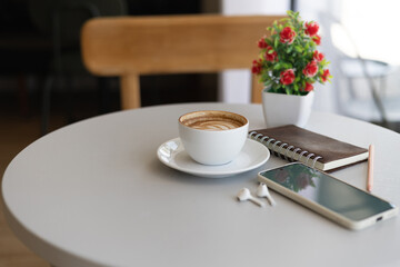 Close-up shot, latte coffee with mobile phone and note book on white table, relax in the morning in cafe before work