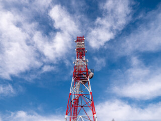 Low-angle view of a red and white telecom tower with antennas and satellite dishes, rising into a...