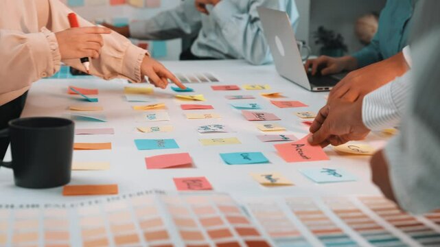 A vibrant collaborative session where diverse professionals engage in color palette creation using sticky notes, laptops, and discussions in a modern workspace setting. SACTR