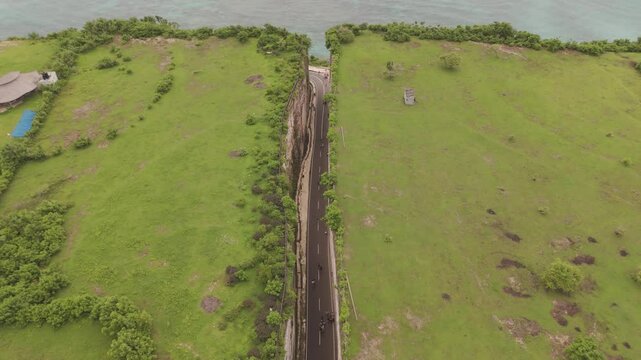 Aerial Descending Shot of Narrow Road Carving Through Valley Leading to Ocean at Tanah Barak, Bali &ndash; Breathtaking Drone Footage of Coastal Landscape and Cliff Passage in Indonesia.