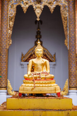 Fototapeta premium golden buddha statue decorated with flower garlands sitting in front of ornate temple entrance, traditional thai architecture with intricate patterns in chiang mai, thailand