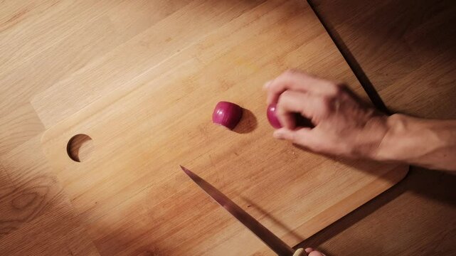 Cutting a red onion on a cutting board, sunlight beaming through window. Wonderful afternoon mood. Top shot of scene. Caucasian hands cutting the onion.