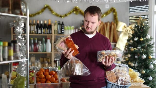 Man in a Christmas supermarket with nut nougat, traditional Italian Panettone bread and delicious panellets desserts. Shopping for the New Year in Europe. High quality 4k footage