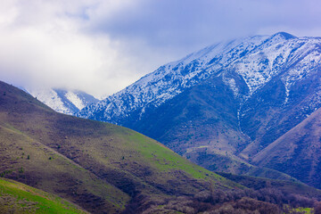 Snow-capped mountain range under a cloudy sky in springtime Kyrgyzstan.