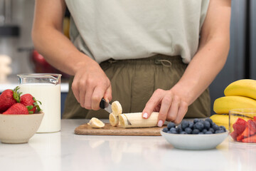 Woman cutting banana. Preparing healthy breakfast with fresh fruits and milk