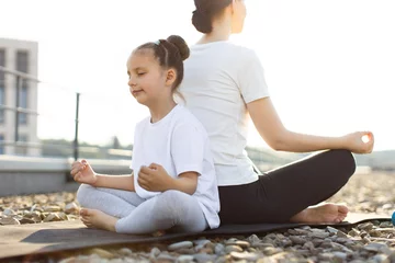 Selbstklebende Fototapeten Young girl and woman meditating in lotus position together outdoors on sunny day. Positive moment portraying relaxation, mindfulness, and family bonding between child and adult © sofiko14