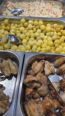 Cooked chicken wings, boiled potatoes and rice with vegetables laying in metal containers, ready for serving