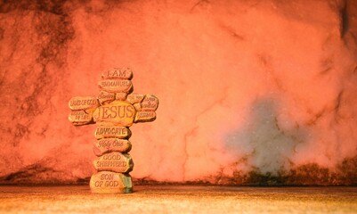 Cross made up of stones with the names of Jesus Christ printed on them. Marble rock background with a light red color.