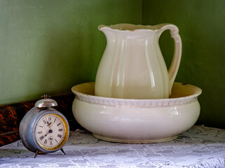Ceramic pitcher and bowl with vintage clock on lace tablecloth in a rustic interior setting