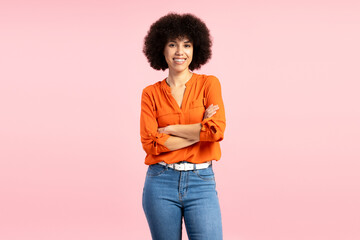 Confident young African American woman smiling with folded arms on pink background