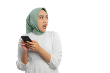 Shocked young Asian woman in green hijab and white blouse holding smartphone and looking aside at copy space, showing amazed expression isolated on transparent background