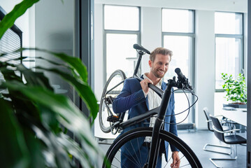 Businessman in a modern office carrying a bike and smiling