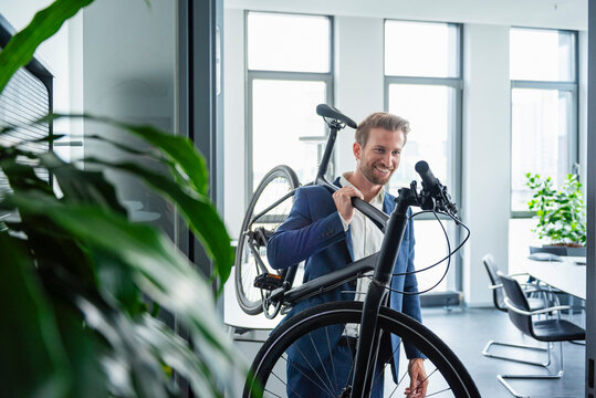 Businessman in a modern office carrying a bike and smiling