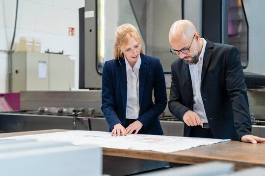 Business professionals discussing blueprints in a production hall