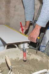 Construction worker measuring a ceramic tile using tape measure and pencil, preparing it for installation during renovation or construction works
