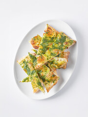 Golden-brown focaccia bread topped with vibrant green pesto, cut into triangular slices and arranged on a white ceramic plate. The crispy crust and airy texture of the bread contrast beautifully with