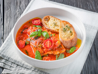 A bowl of lasagna soup with a rich tomato broth, cherry tomatoes, fresh basil, and toasted bread slices. Served in a white bowl on a textured light grey background. A comforting and hearty Italian