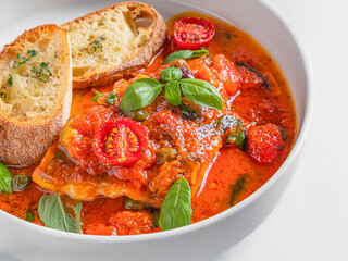 A bowl of lasagna soup with a rich tomato broth, cherry tomatoes, fresh basil, and toasted bread slices. Served in a white bowl on a textured light grey background. A comforting and hearty Italian