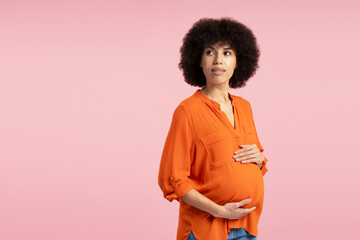 Attractive African American pregnant woman holding belly and looking away on pink background