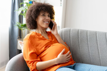 Pregnant woman relaxing on sofa and talking on smartphone